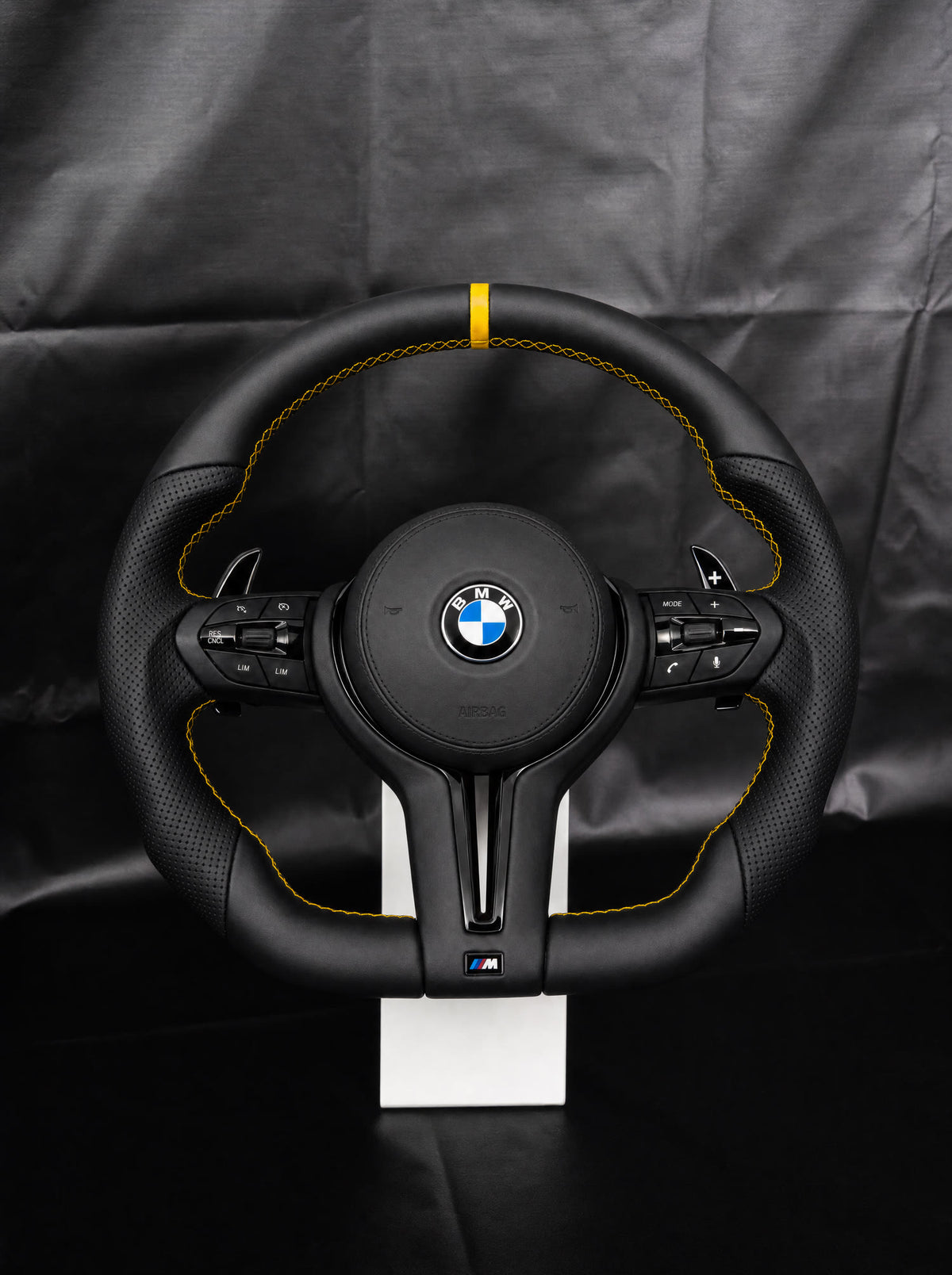 Volante BMW de cuero con franja y costura amarillas sobre peana