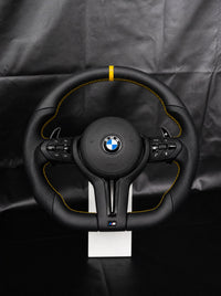 Volante BMW de cuero con franja y costura amarillas sobre peana
