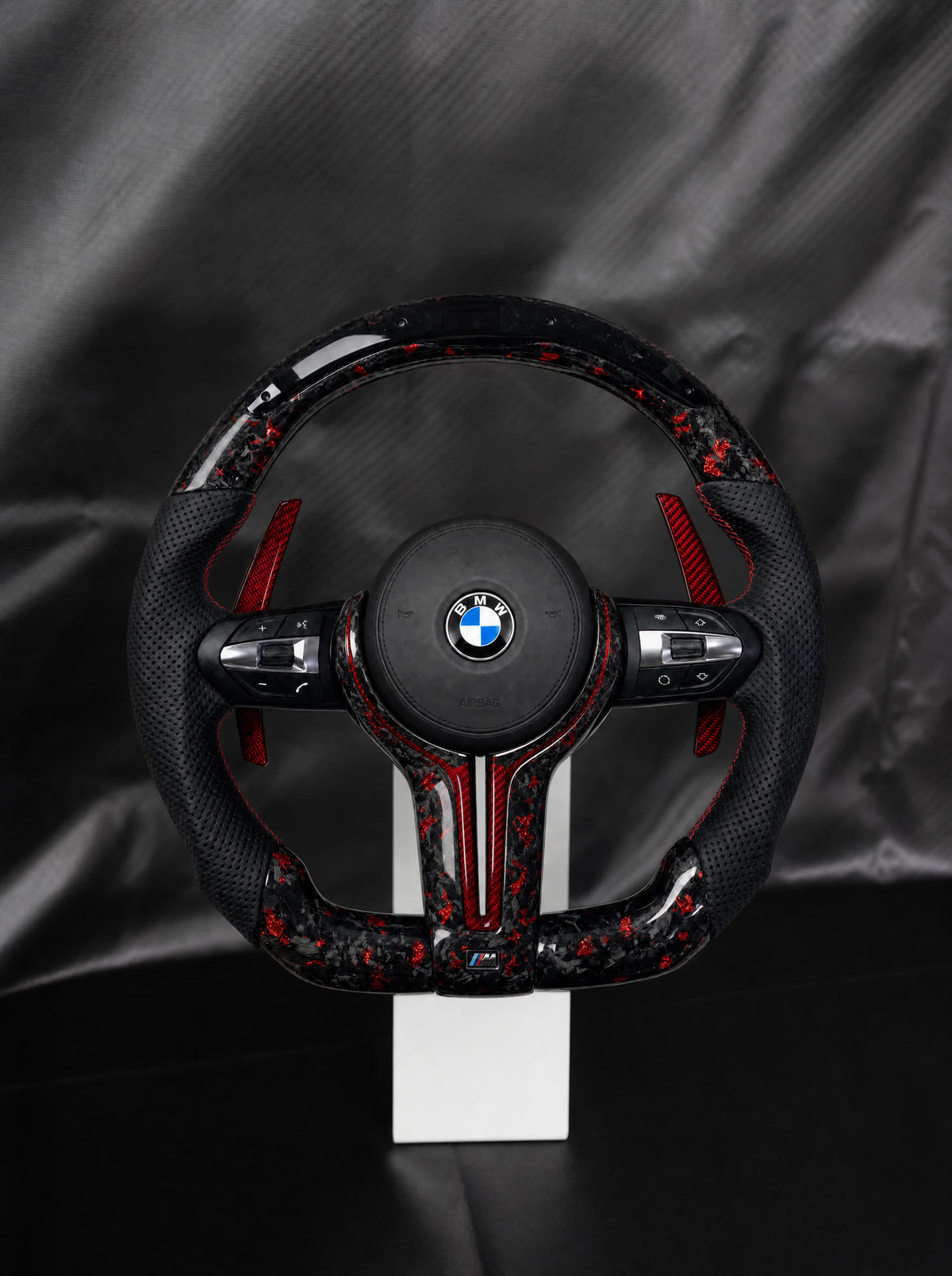 Volante BMW de fibra de carbono forjada roja con airbag sobre peana